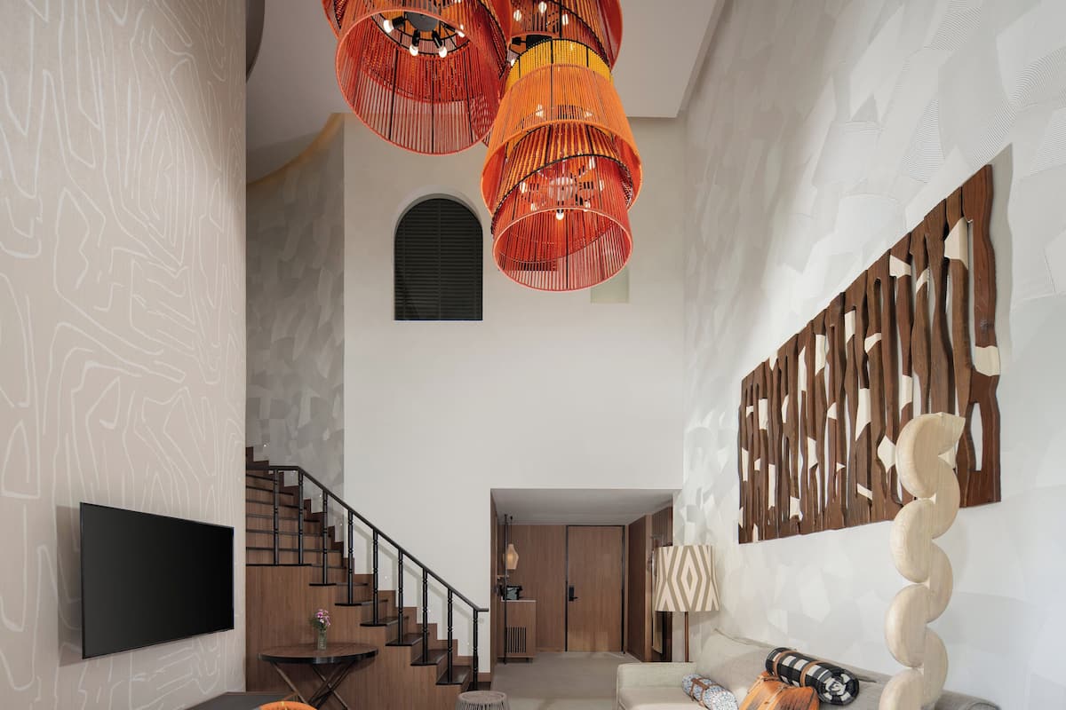 Un salón espacioso con una escalera, un televisor de pantalla plana, un sillón colorido, un sofá gris y una mesa de centro de madera.