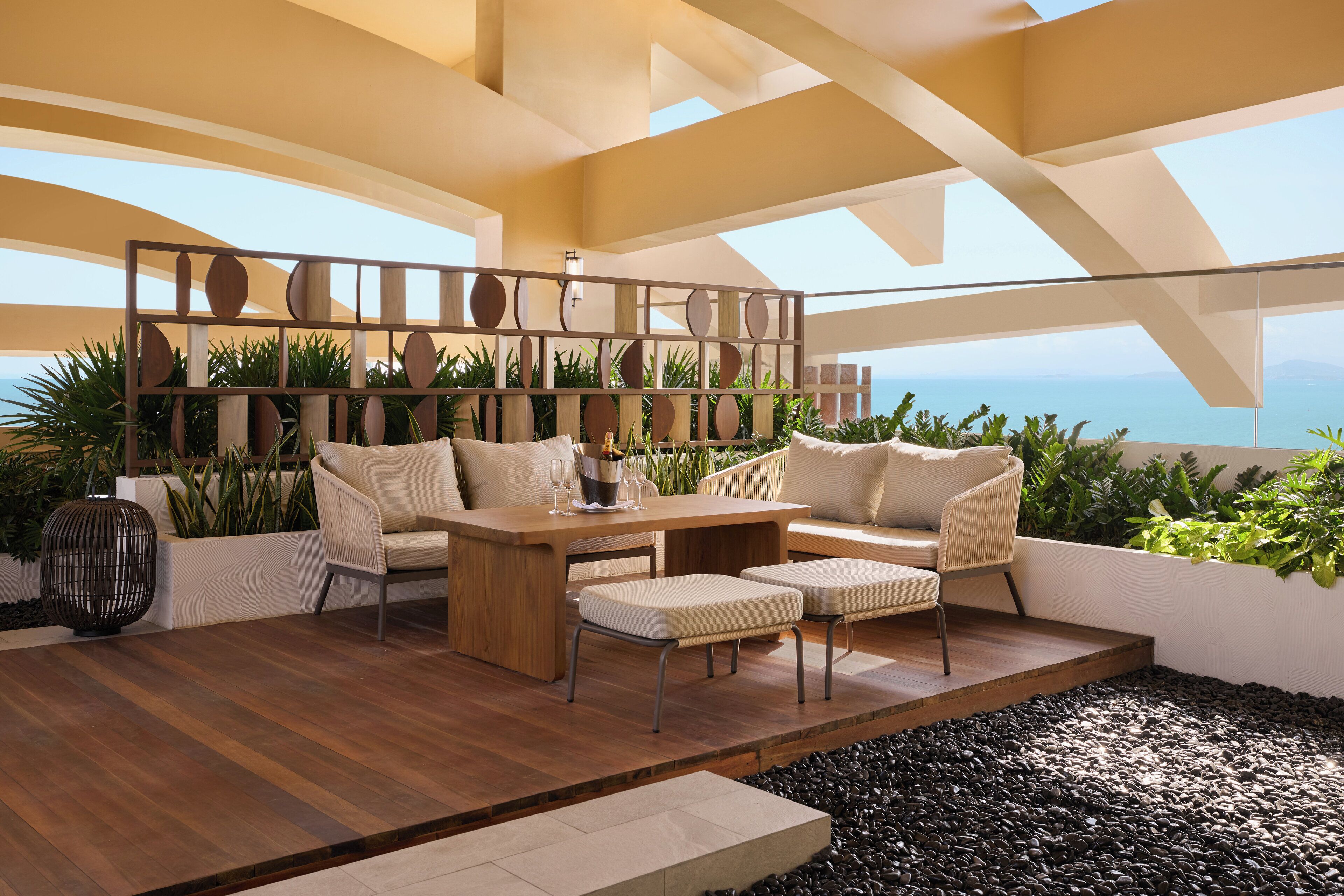 A modern outdoor seating area with a wooden table, cushioned chairs, and a decorative metal partition.