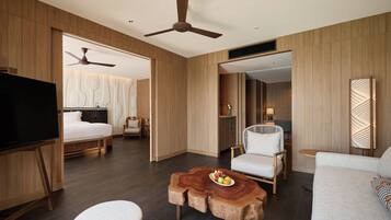 A modern hotel room with a bed, a TV, a ceiling fan, a wooden coffee table with fruit, and a sofa.