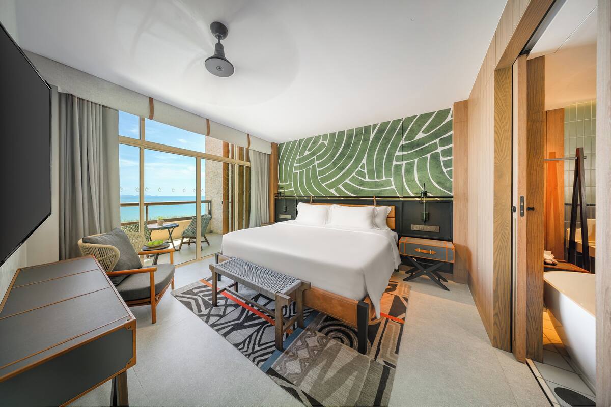 Habitación de hotel moderna con una cama grande, un escritorio, una silla y un balcón con vistas.
