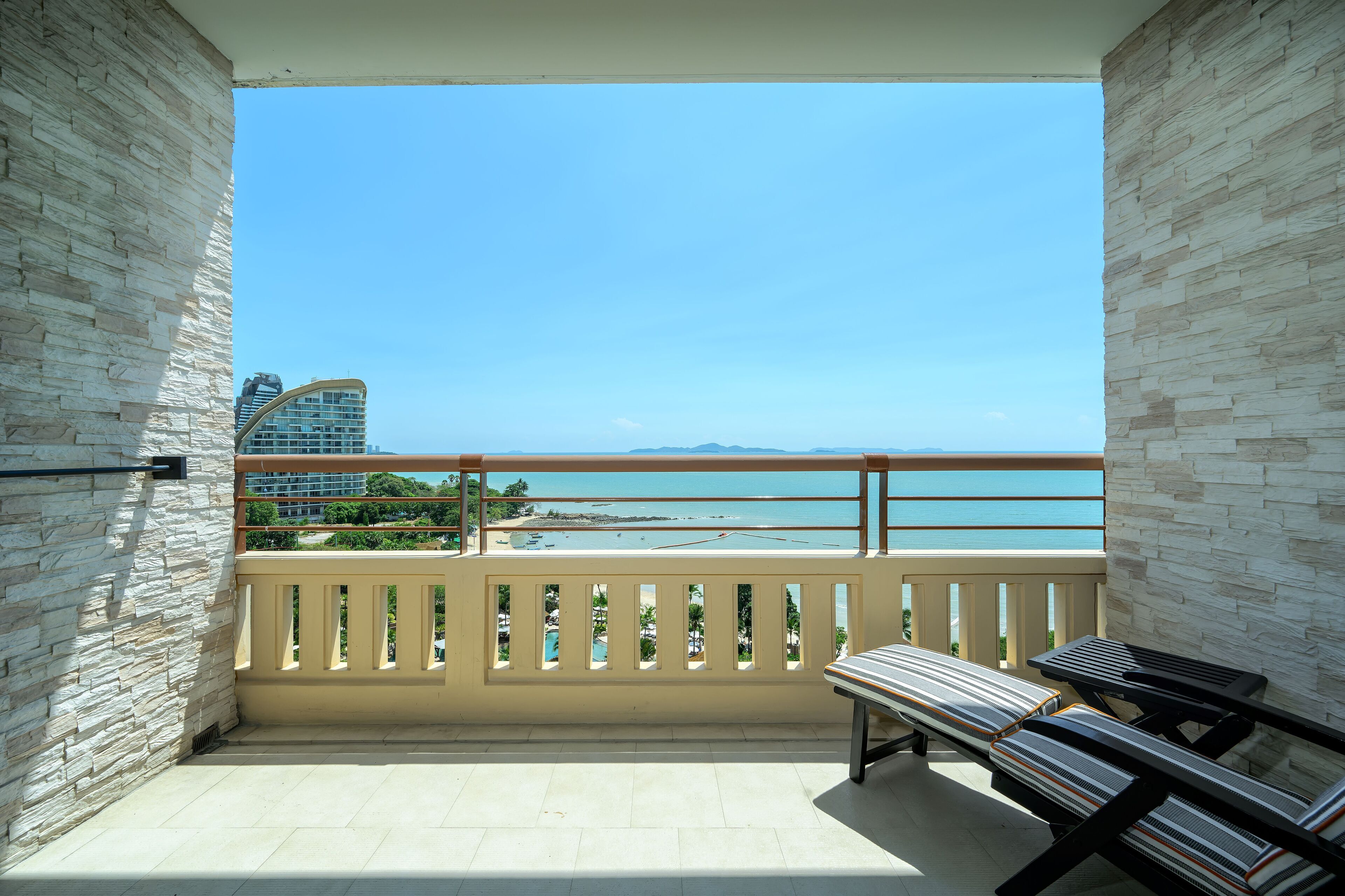 A balcony with a view of the beach and ocean, featuring a railing and a bench.