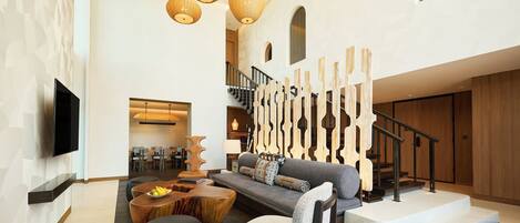 A spacious living area with a modern sofa, wooden accents, a staircase, and a flat-screen TV mounted on the wall.