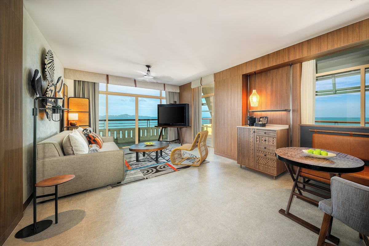 Una habitación de hotel moderna con balcón, sofá, mesa de comedor y televisor.