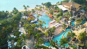 Un resort con varias piscinas, palmeras y una playa.