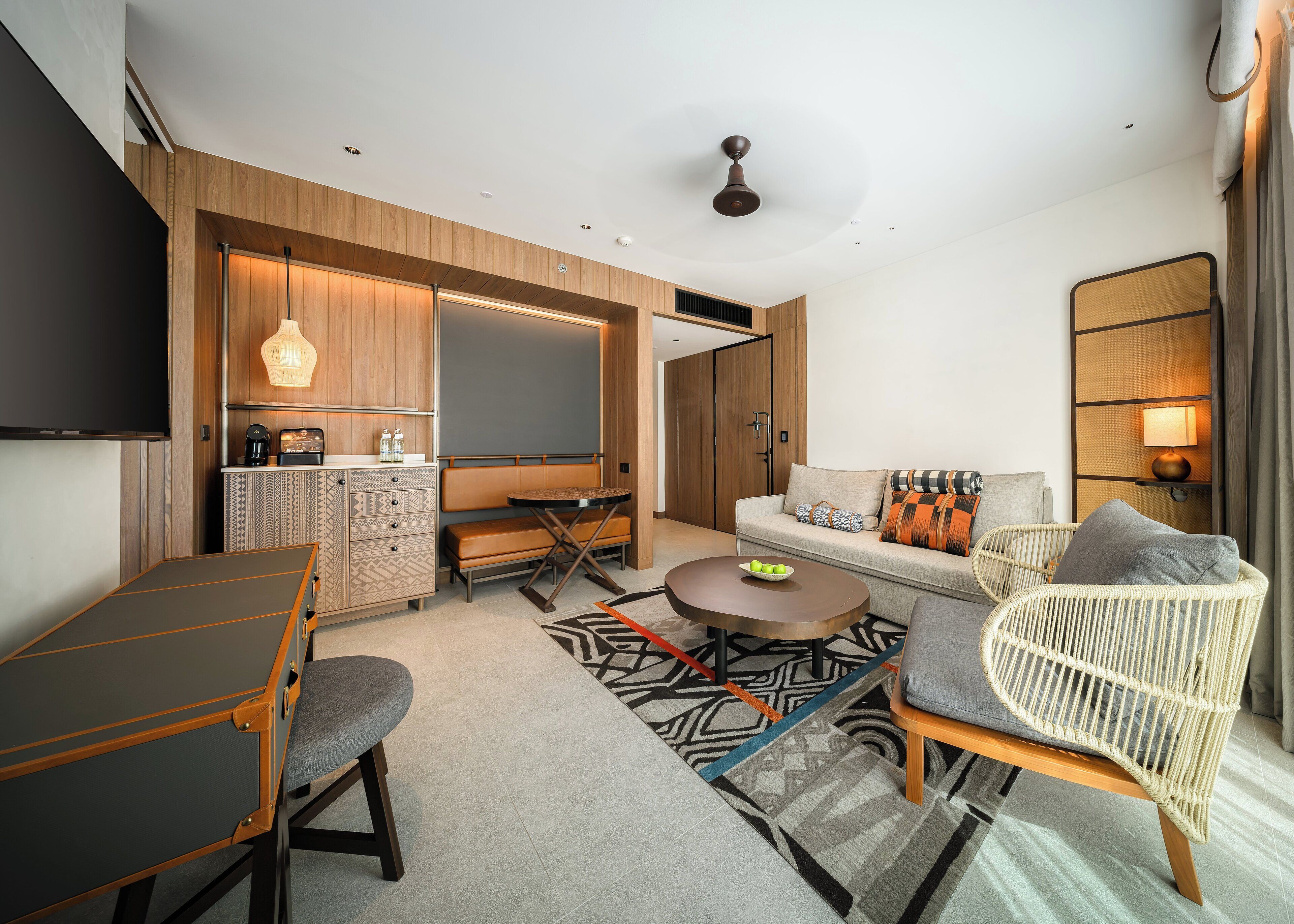 A modern hotel room with a dining table, sofa, and a TV.