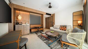 A modern hotel room with a dining table, sofa, and a TV.