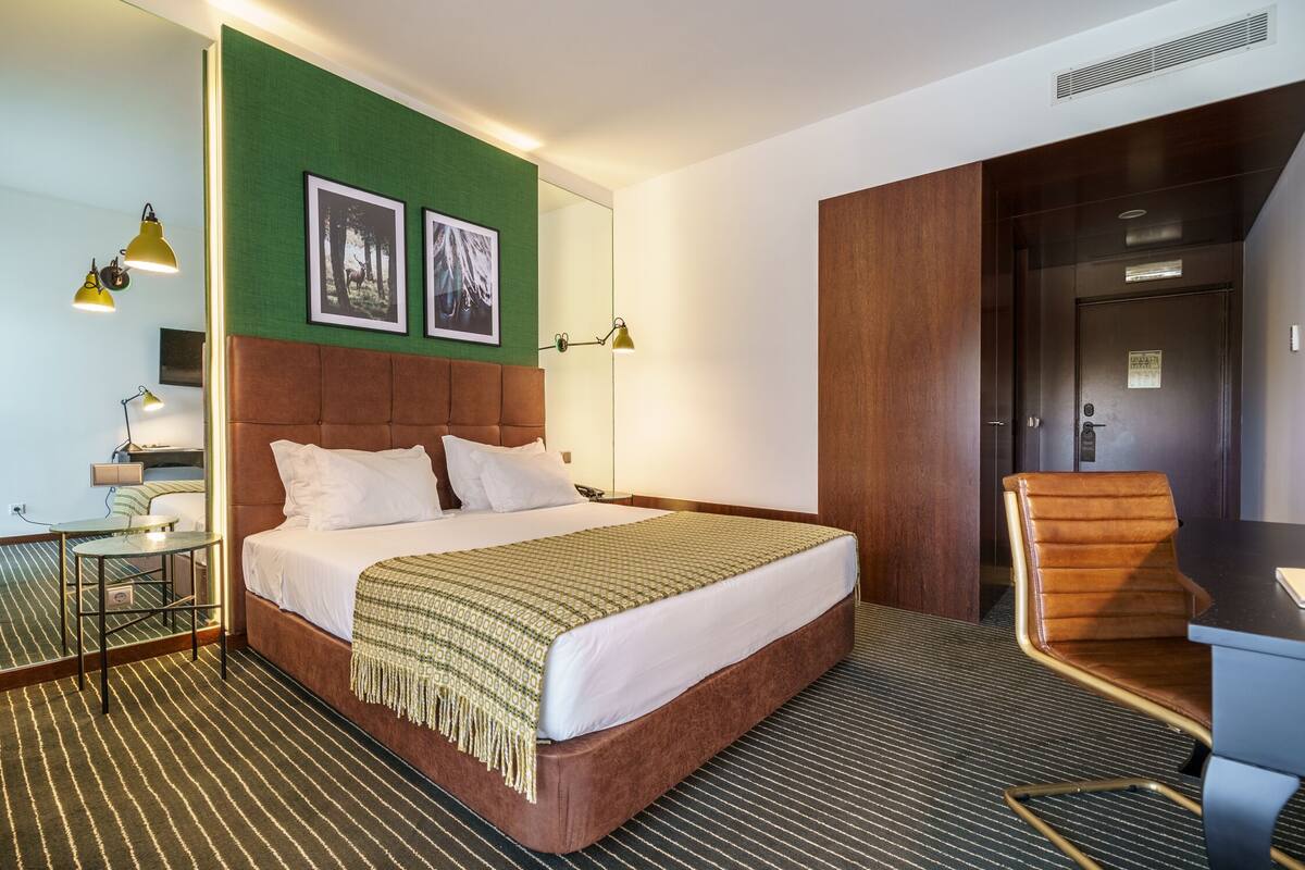 A hotel room with a large bed, a desk, a chair, and two framed pictures on the wall.