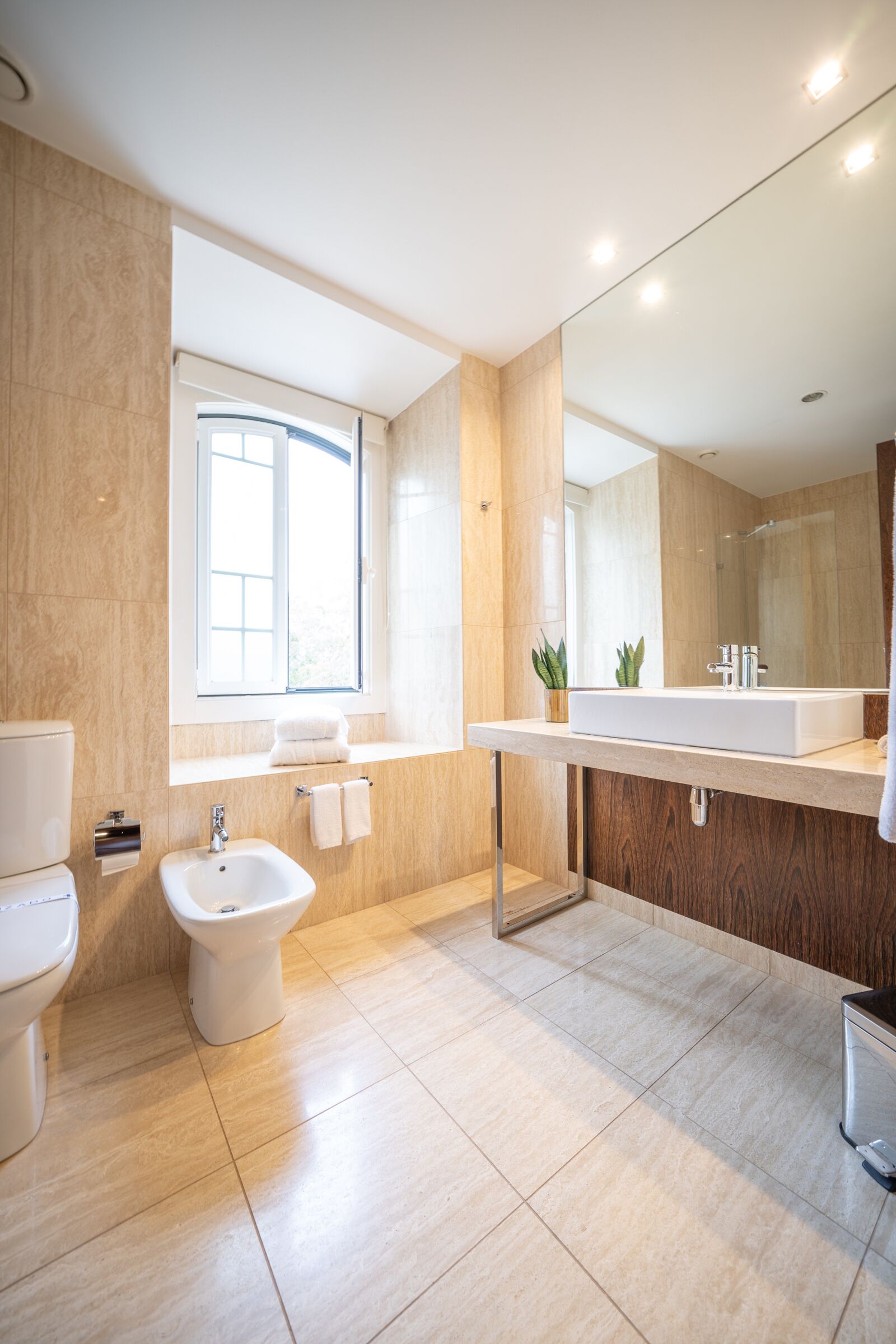 A modern bathroom with a toilet, bidet, sink, and mirror.