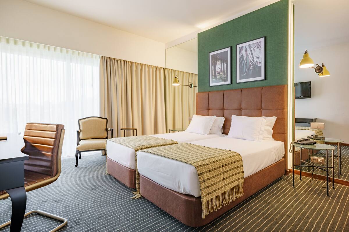 A hotel room with a large bed, two bedside tables, a chair, a desk, and a TV.