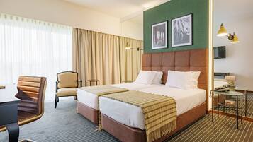 Ein Hotelzimmer mit einem großen Bett, zwei Nachttischen, einem Sessel, einem Schreibtisch und einem Fernseher.