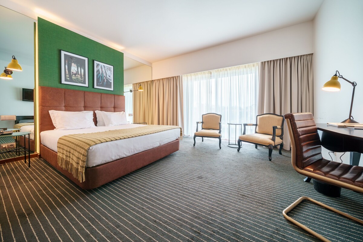 A hotel room with a large bed, two chairs, a desk, and a lamp.