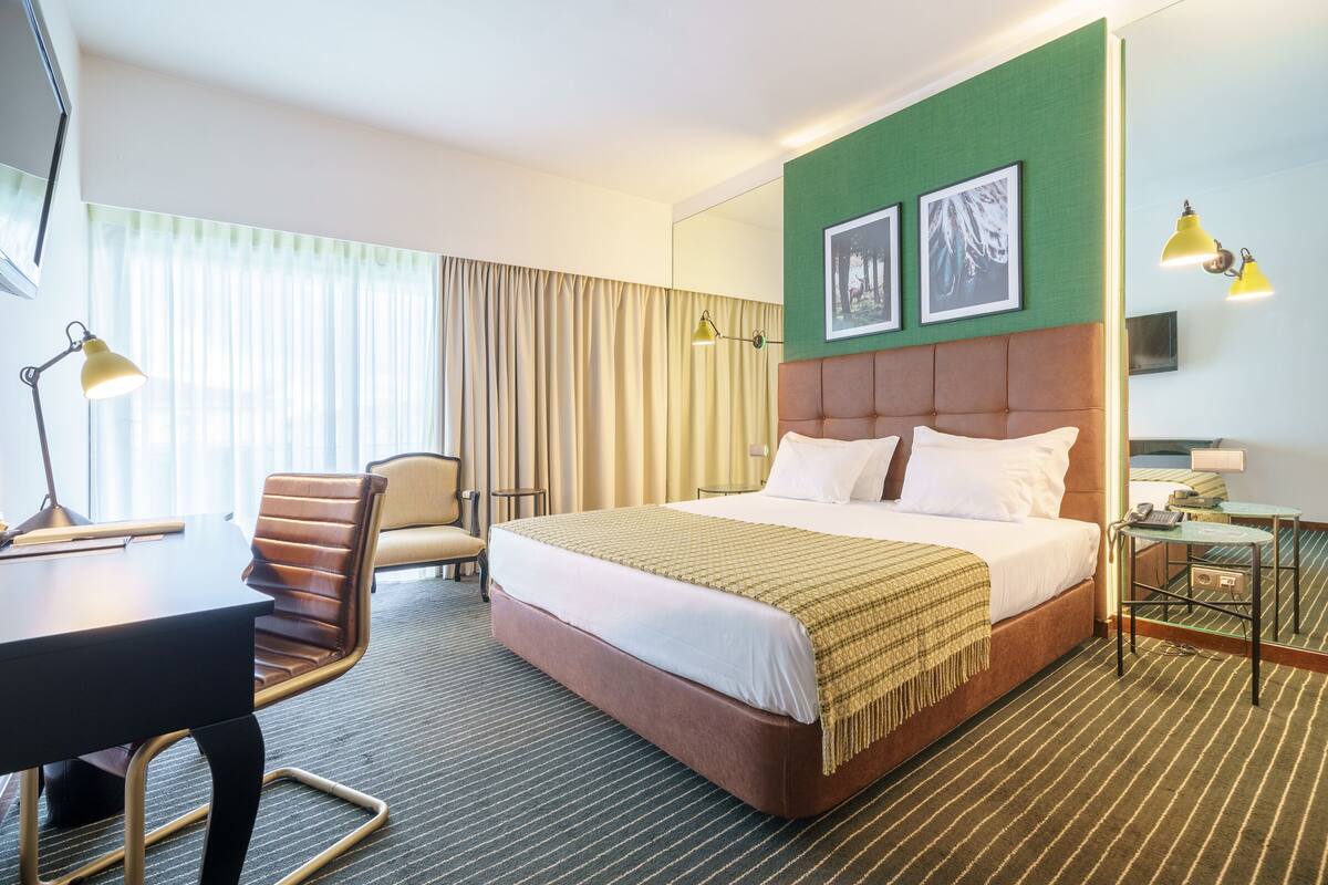 A hotel room with a large bed, a desk, a chair, and a small table.
