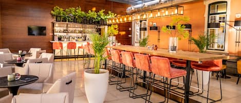 A modern bar area with a long counter, multiple bar stools, and potted plants.