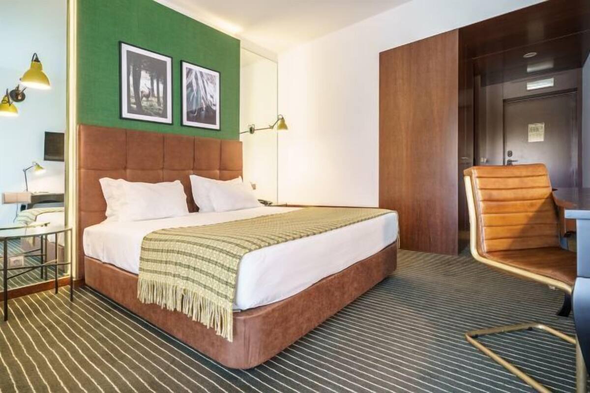 A hotel room with a bed, a chair, a desk, and a mirror.