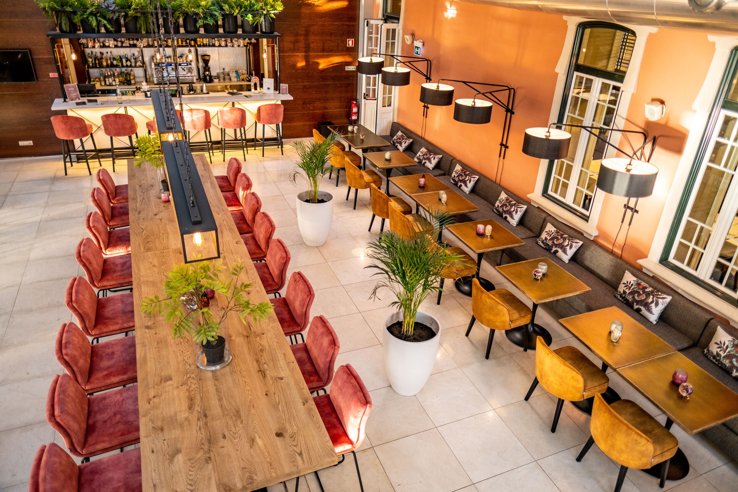 Un restaurant spacieux doté de plusieurs espaces de restauration, notamment de longues tables communes et des tables individuelles, le tout agrémenté de plantes en pot et d’un éclairage moderne.