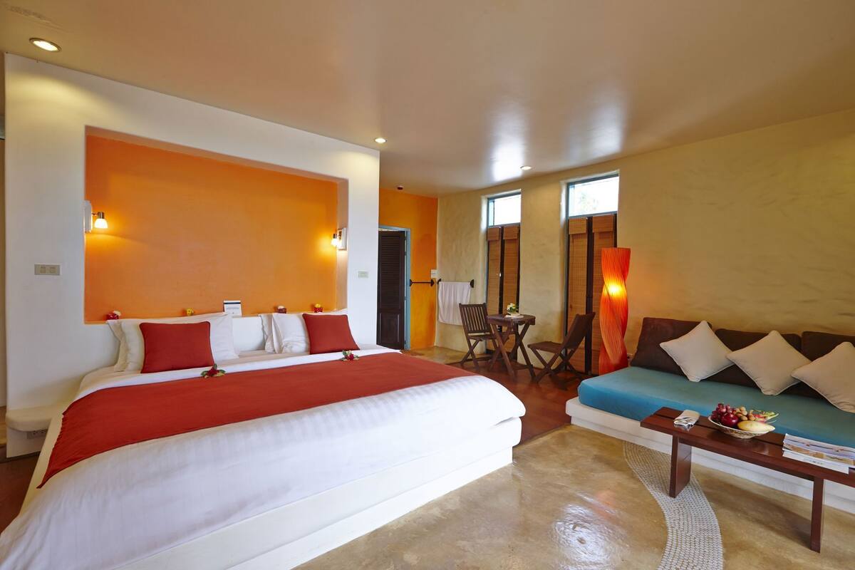 Une chambre d’hôtel avec un grand lit, un canapé, une petite table avec des fruits et une chaise.