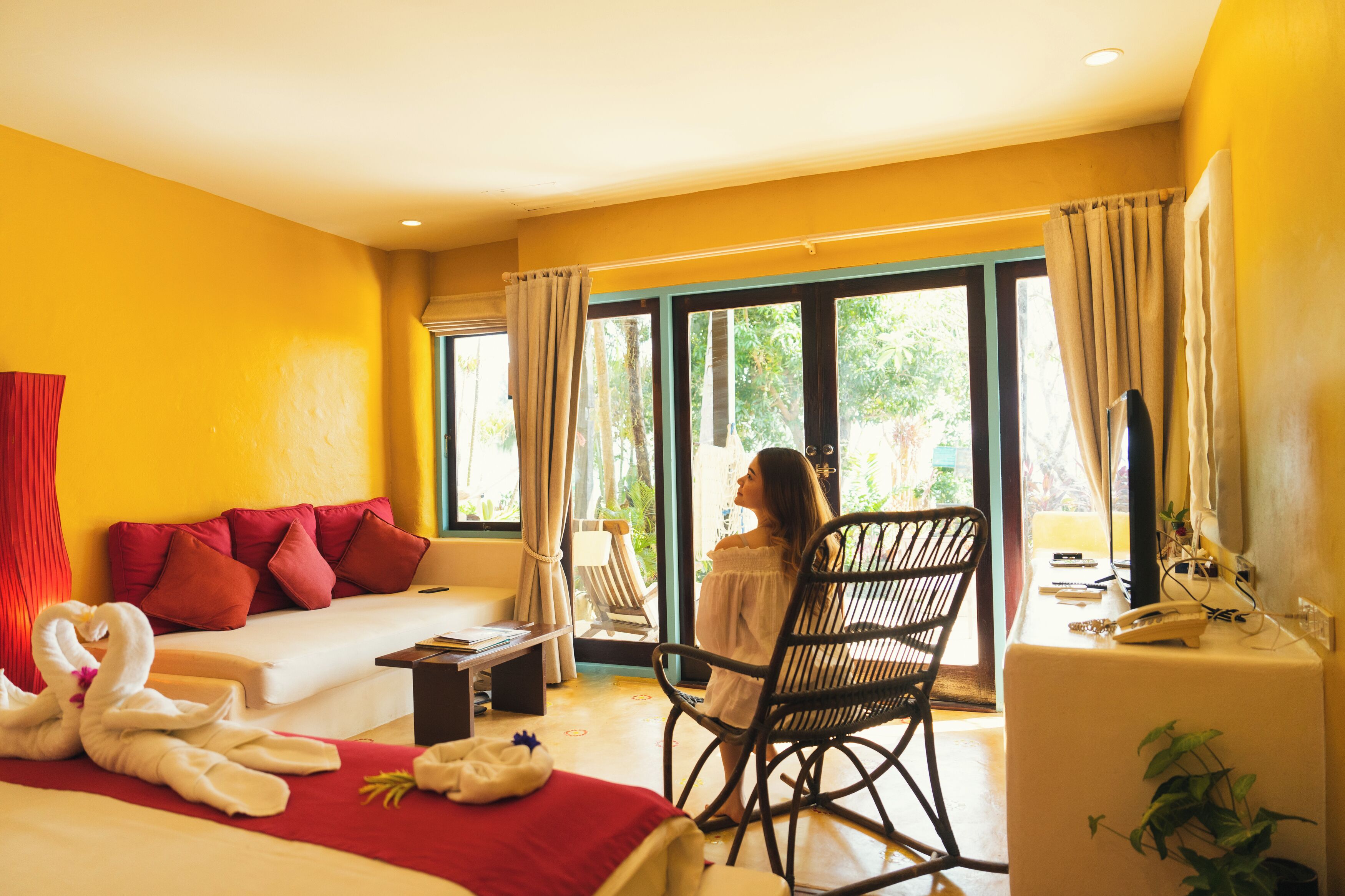 Habitación de hotel con cama, sofá, sillón mecedor, escritorio y una ventana grande con cortinas.