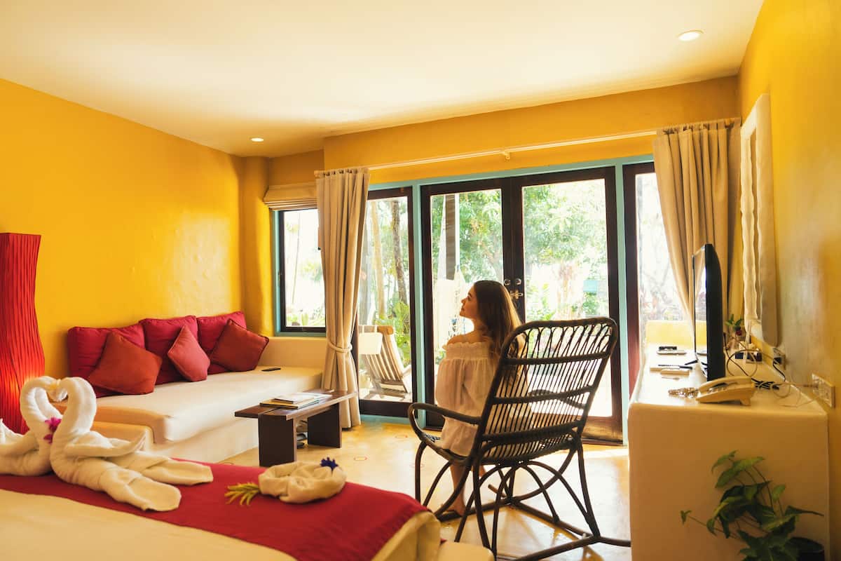 Habitación de hotel con cama, sofá, sillón mecedor, escritorio y una ventana grande con cortinas.