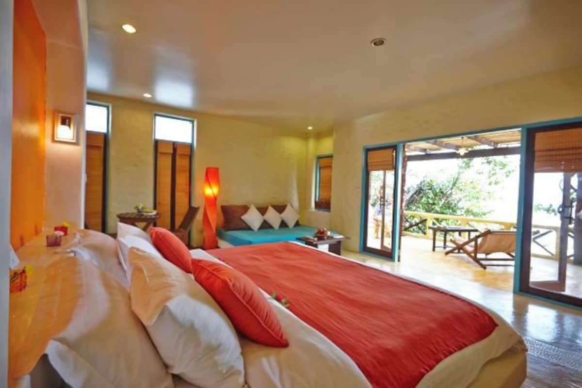Een hotelkamer met een groot bed, een kleintje tafeltje en een balkon met tuinmeubilair.