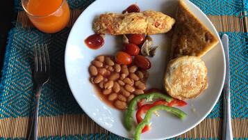 A plate with eggs, toast, beans, tomatoes, mushrooms, and a green pepper on a woven placemat.
