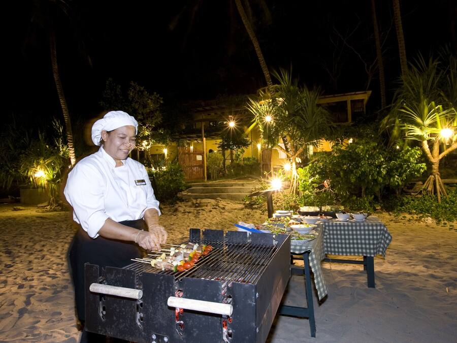 A chef grilling outdoors at night with a table set for dining nearby.