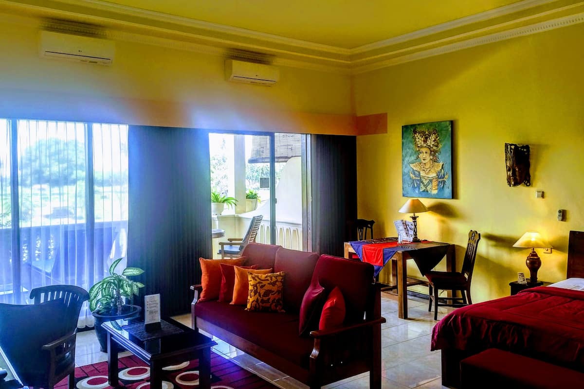Une chambre d’hôtel avec un canapé rouge, un lit, une table à manger avec des chaises et un balcon agrémenté de plantes.