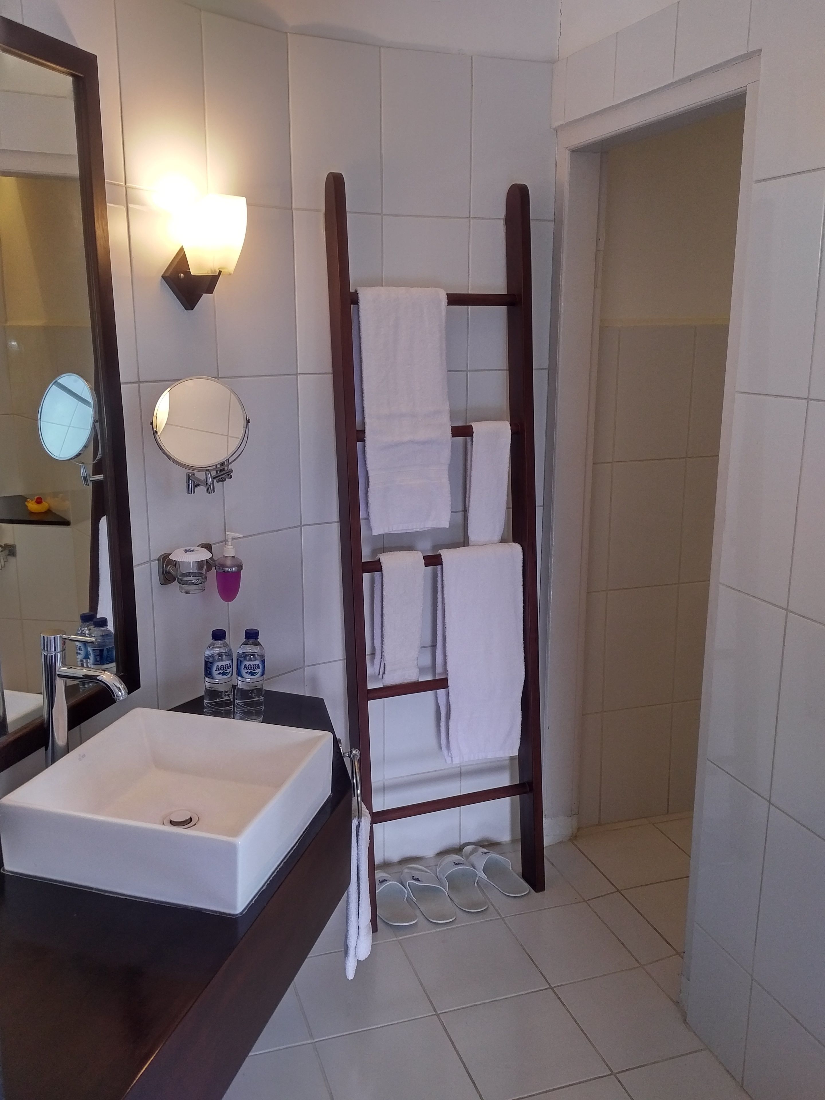 A bathroom with a white sink, a mirror, a towel rack, and a pair of slippers on the floor.