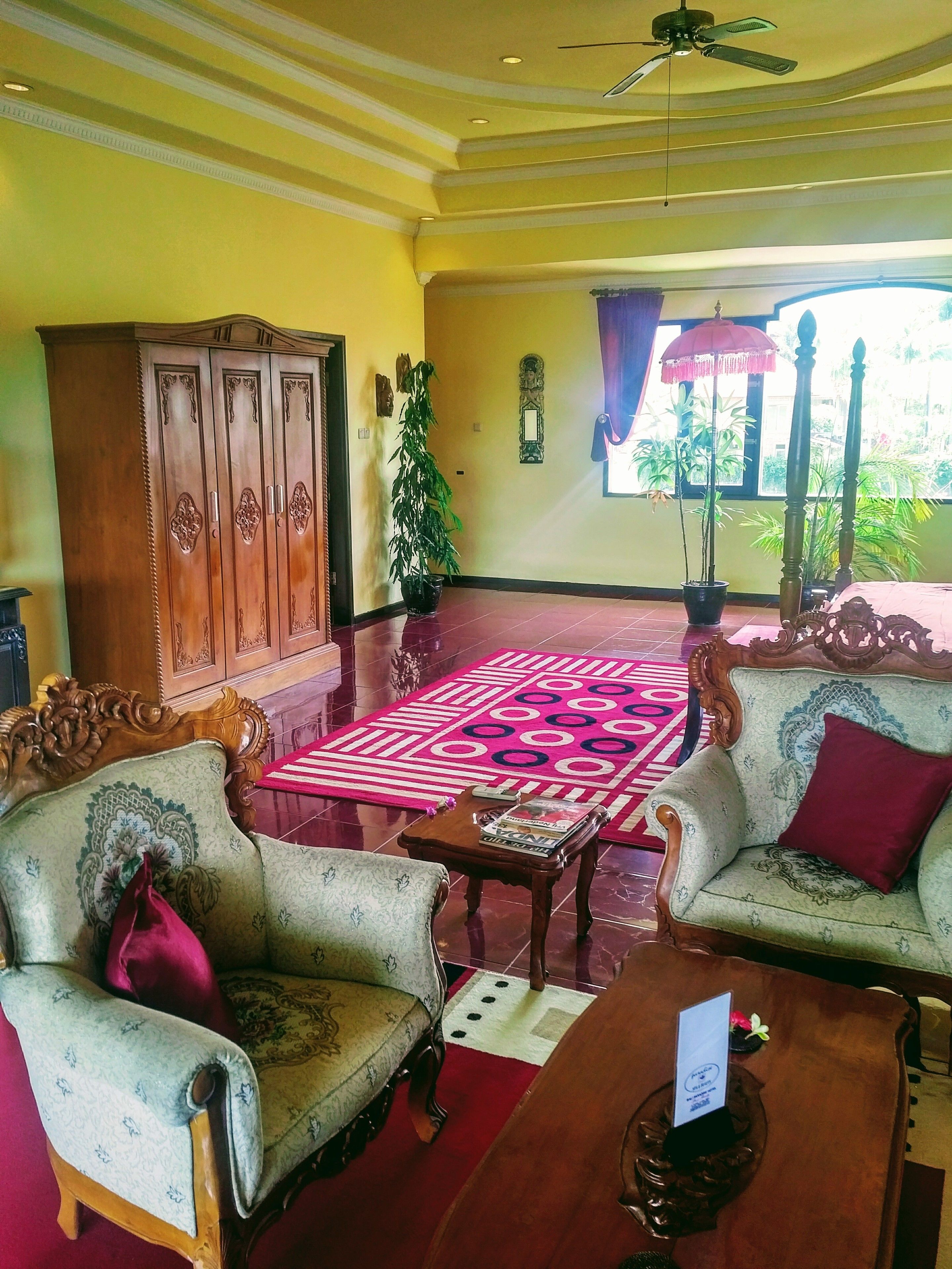 Una habitación tradicional con un aparador de madera, dos sillas decorativas, un tapete estampado y un ventilador de techo.