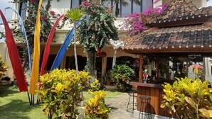 Een hotel met een traditioneel betegeld dak, een overdekt terras en een tuin met diverse planten en bloemen.