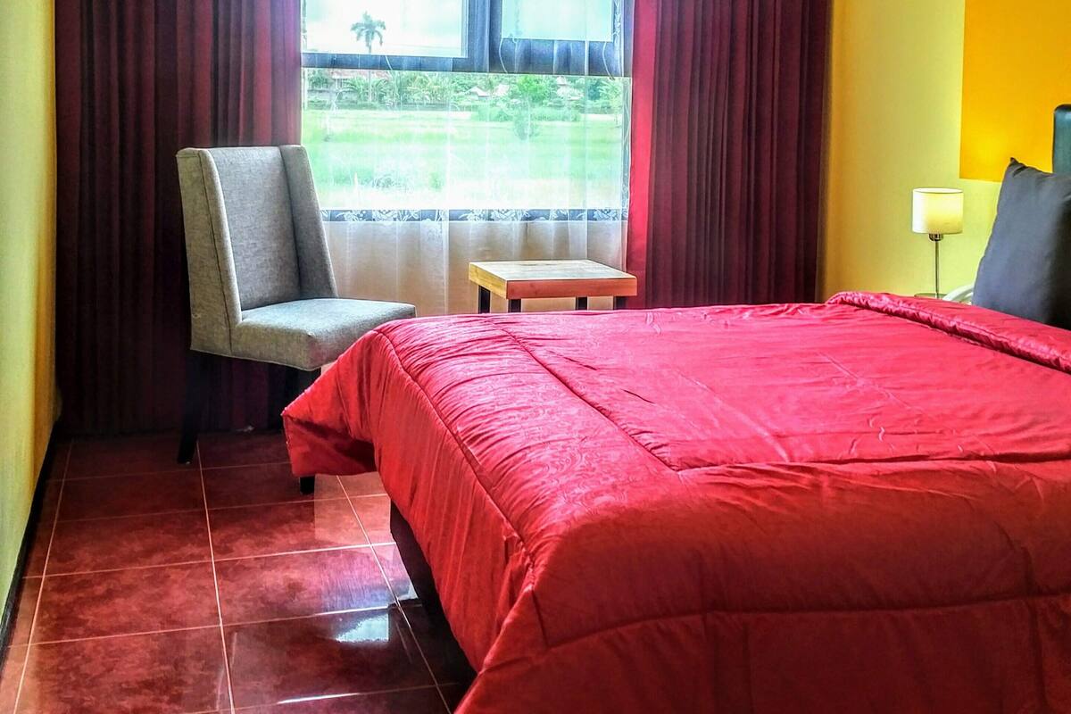 Une chambre d’hôtel avec un lit, une chaise, une petite table et une fenêtre avec des rideaux.