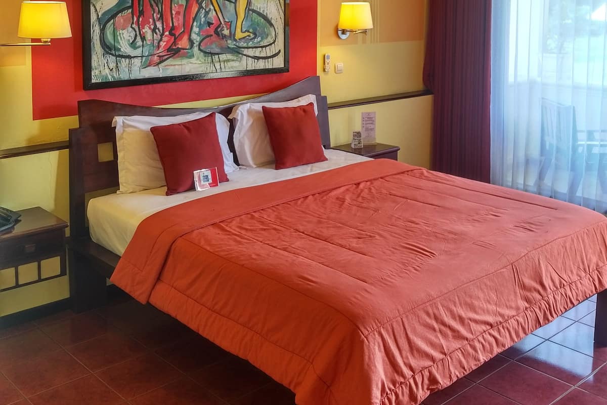 Une chambre d’hôtel avec un lit, un tableau au mur, deux lampes de chevet et une fenêtre avec des rideaux.