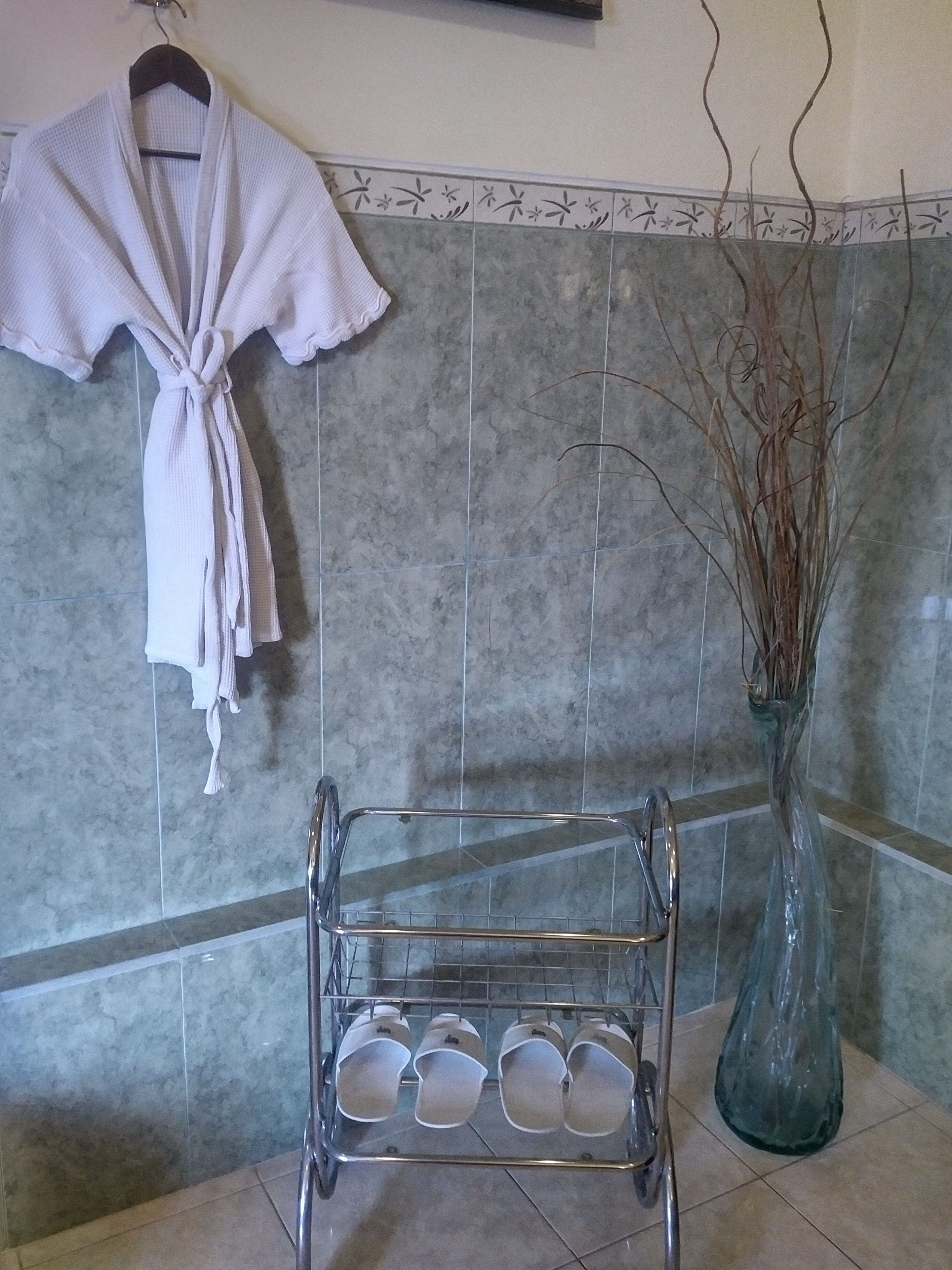 Un baño con un perchero para toallas, un estante de vidrio con tazas y un jarrón con plantas secas.