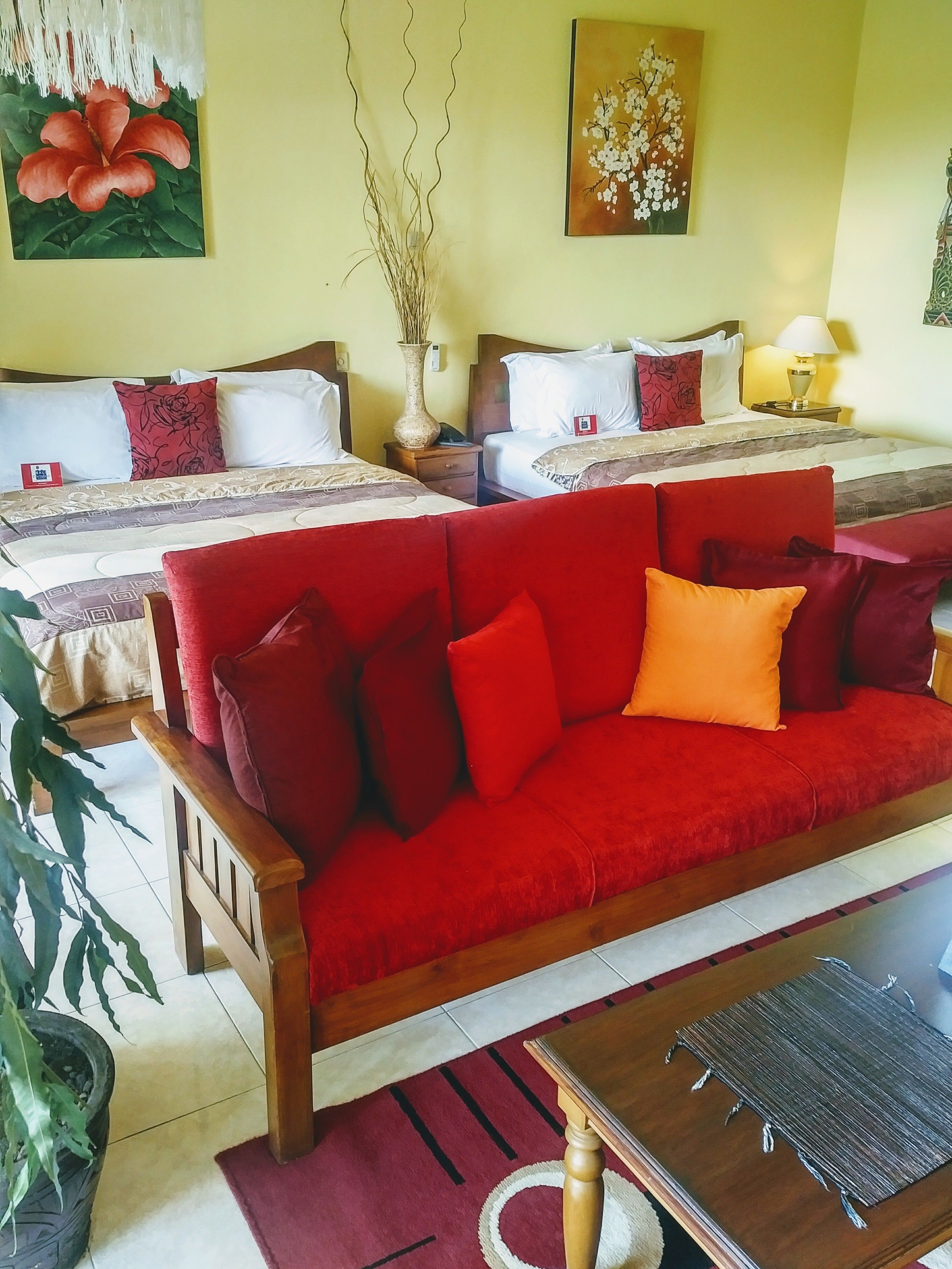 A hotel room with two beds, a red sofa, a wooden coffee table, and a potted plant.