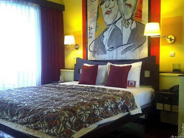 Une chambre d’hôtel avec un grand lit, deux lampes de chevet, une horloge murale et un tableau au-dessus du lit.