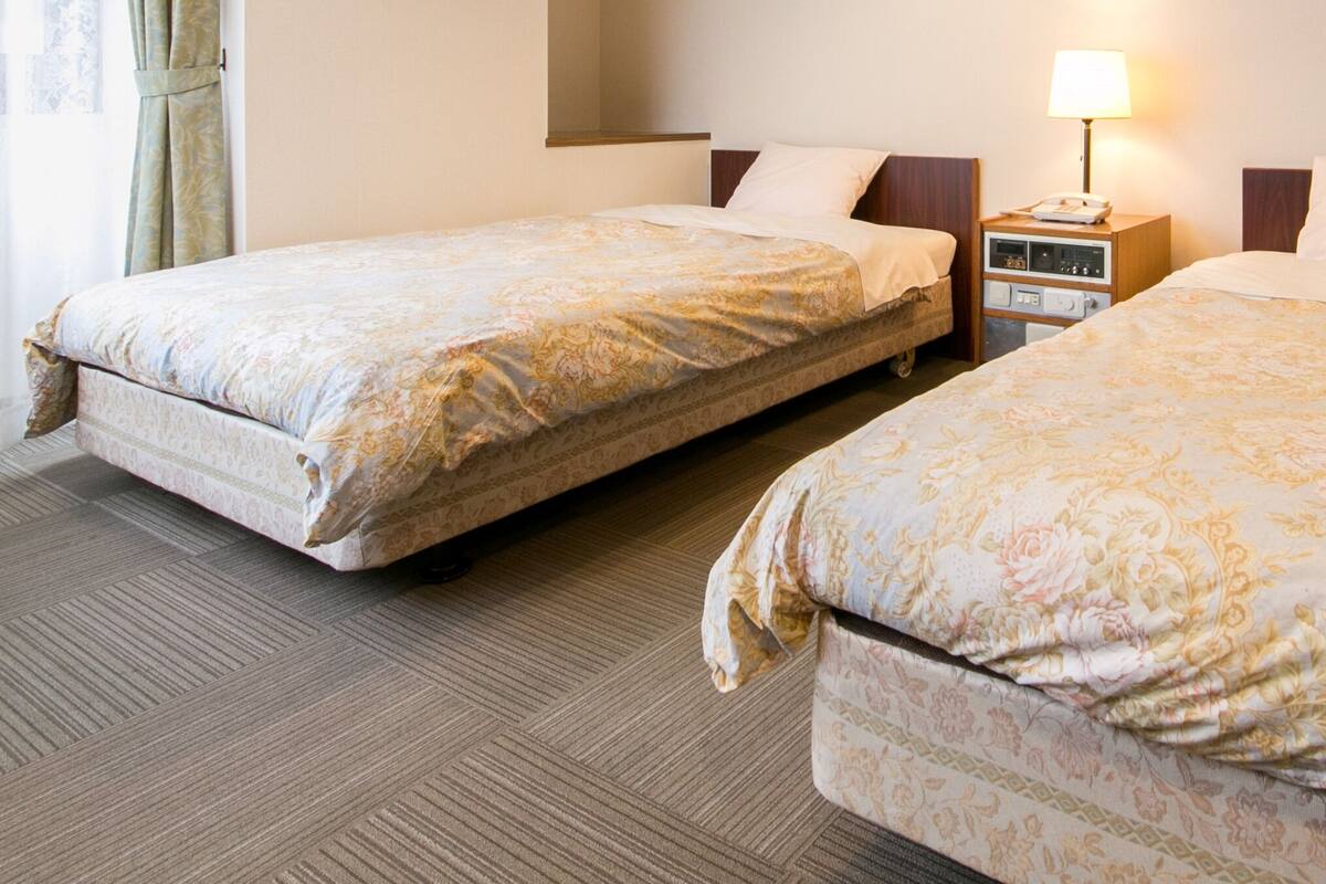 Two single beds with floral bedding, a bedside table with a lamp, and a carpeted floor.