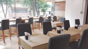 A restaurant with multiple tables and chairs, a window with a view of trees and buildings, and a clean, modern interior. - Hotel Ohedo (Tokyo)