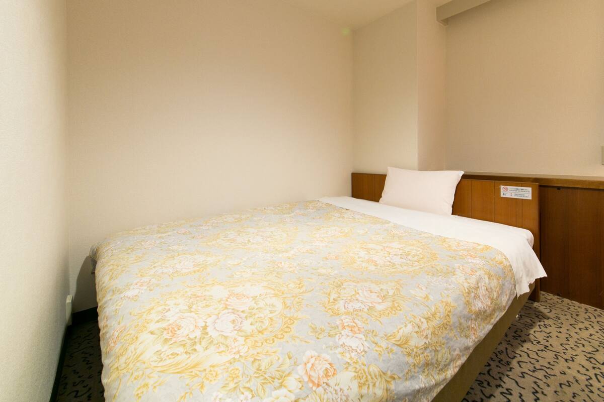 A hotel room with a bed, a wooden headboard, and a sign on the wall.