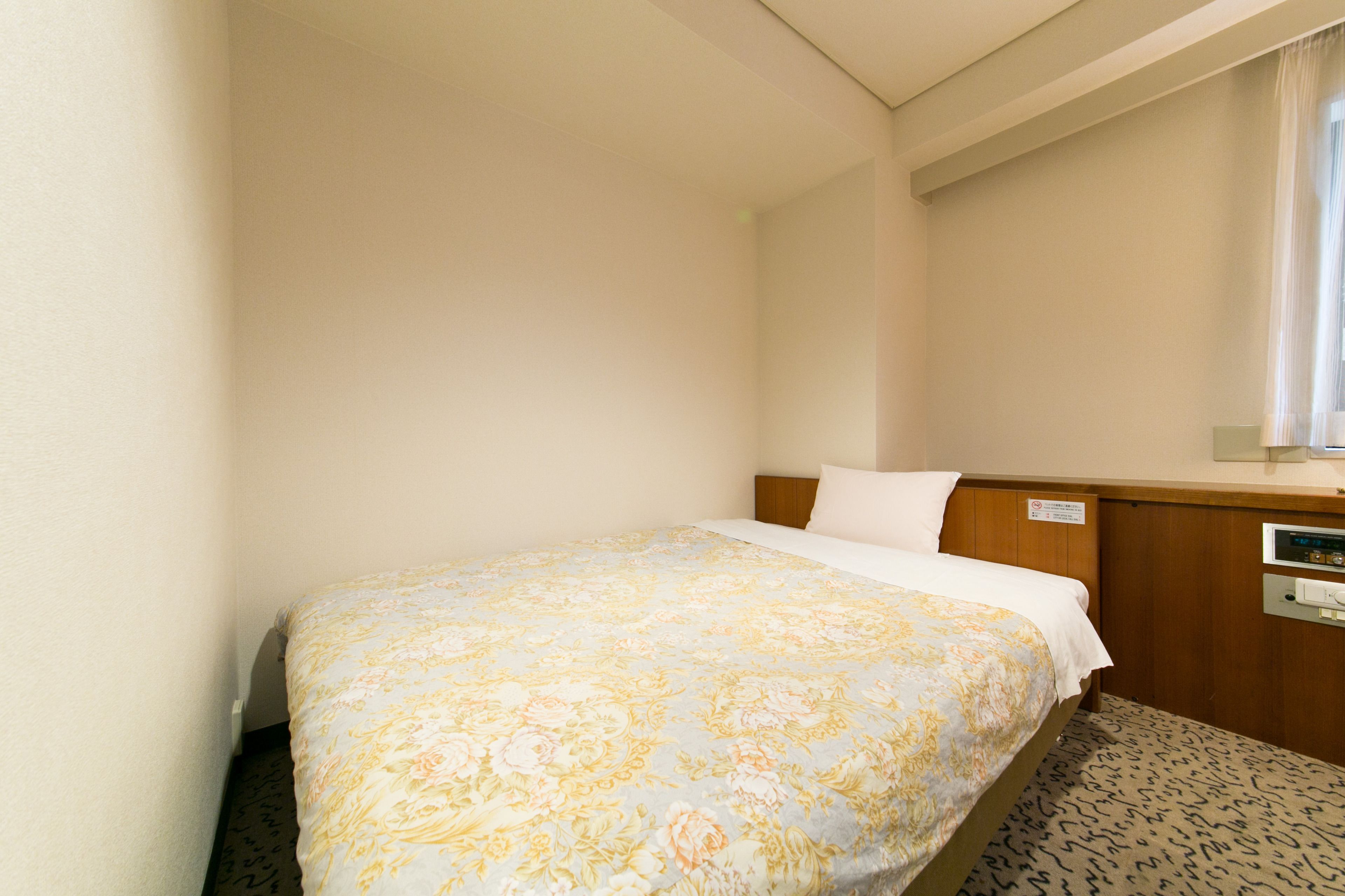 A hotel room with a bed, a wooden headboard, a nightstand, and a window with curtains.