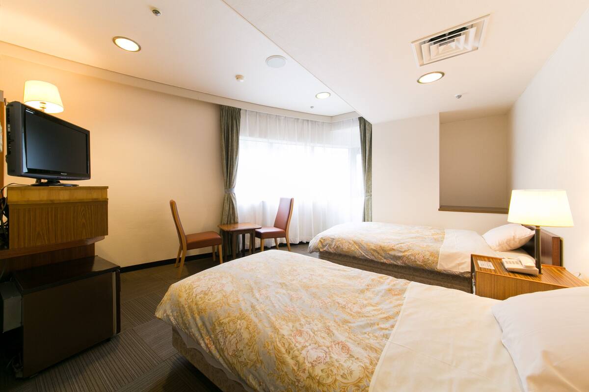A hotel room with two beds, a television, a desk, and a chair.