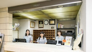 A reception desk with three staff members, a clock, framed certificates, and a bookshelf. - Hotel Ohedo (Tokyo)