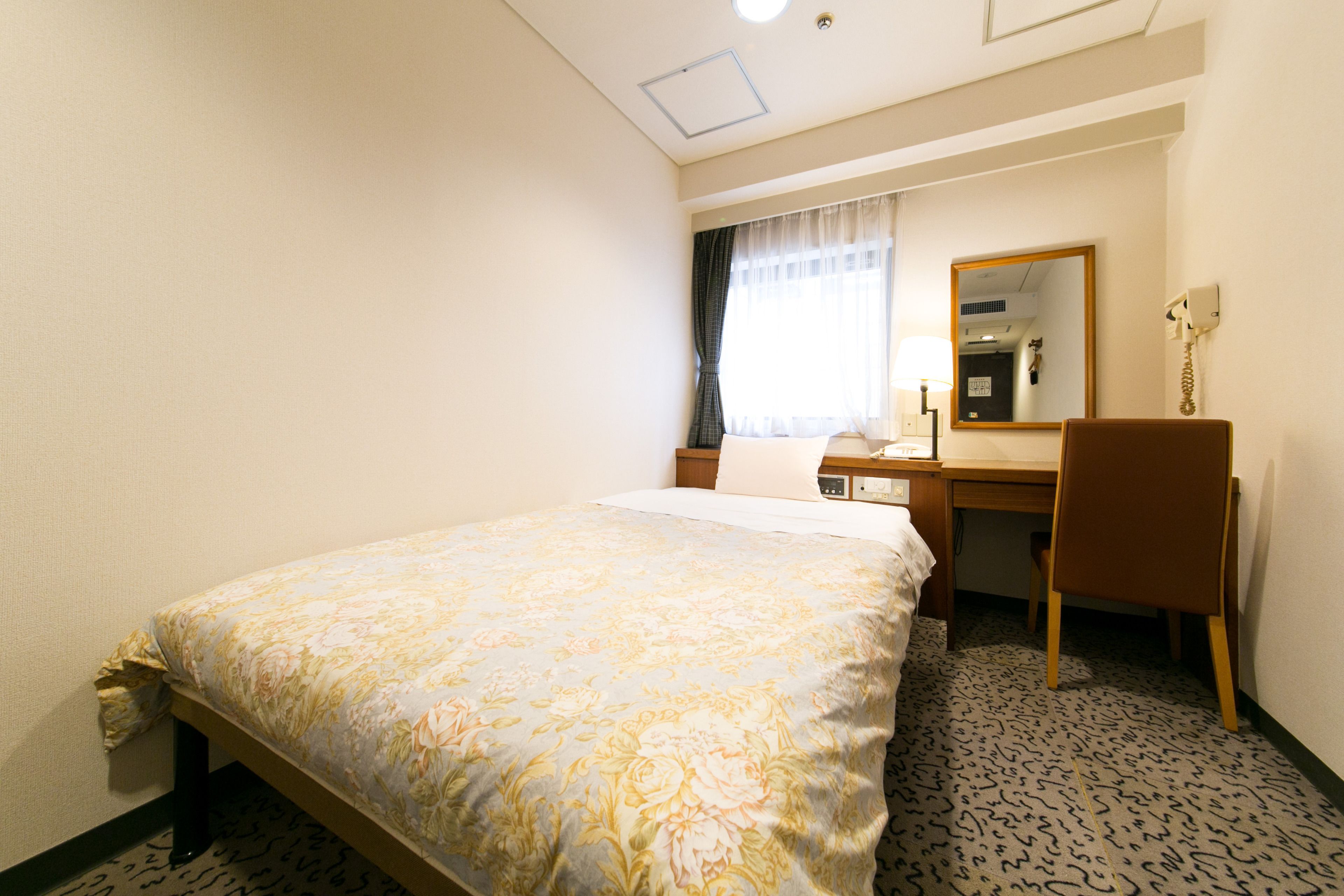 Une chambre d’hôtel comprenant un lit, un bureau, une chaise, un miroir et un téléphone.