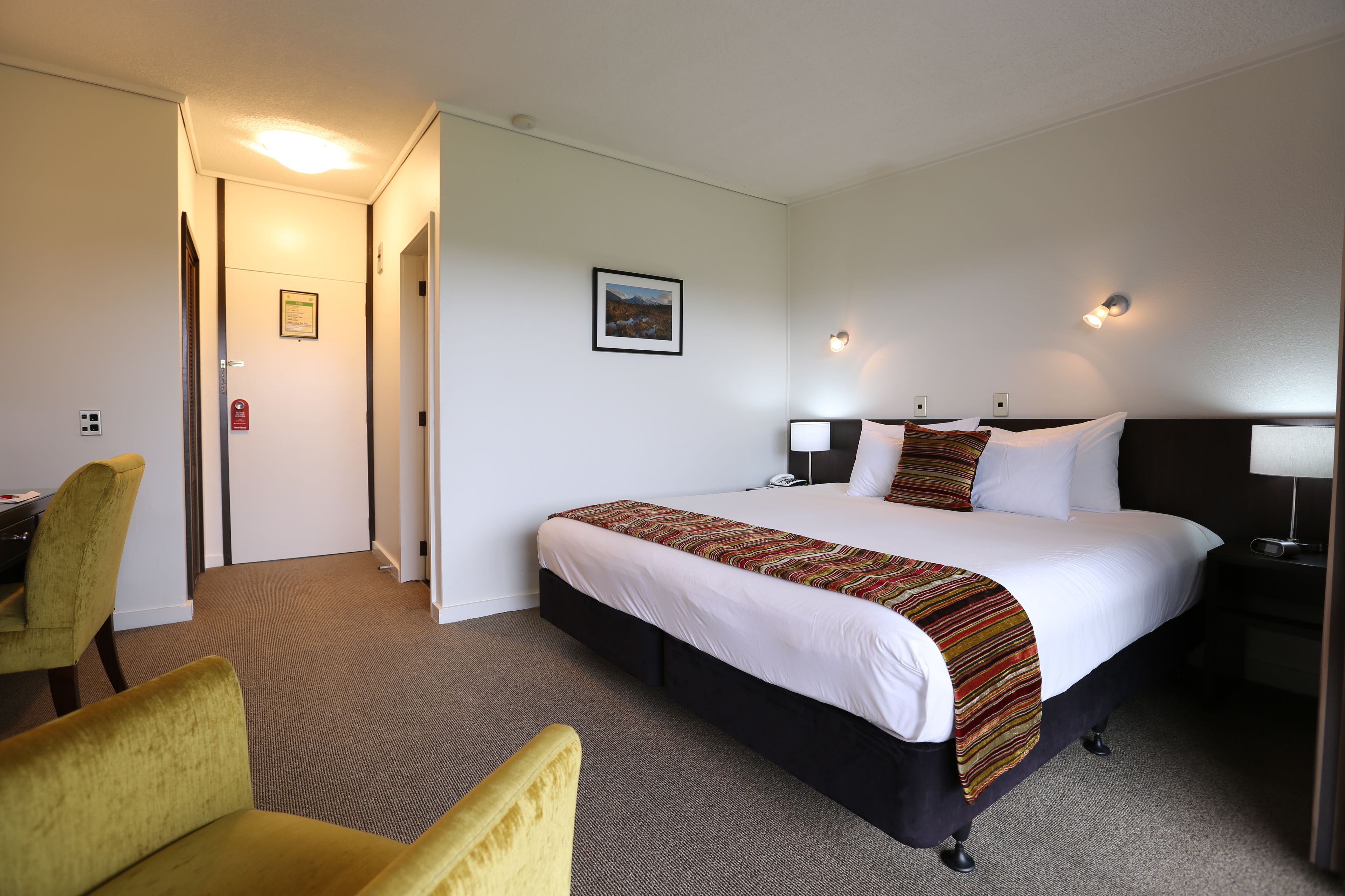 A hotel room with a bed, bedside tables, a desk, and a chair.