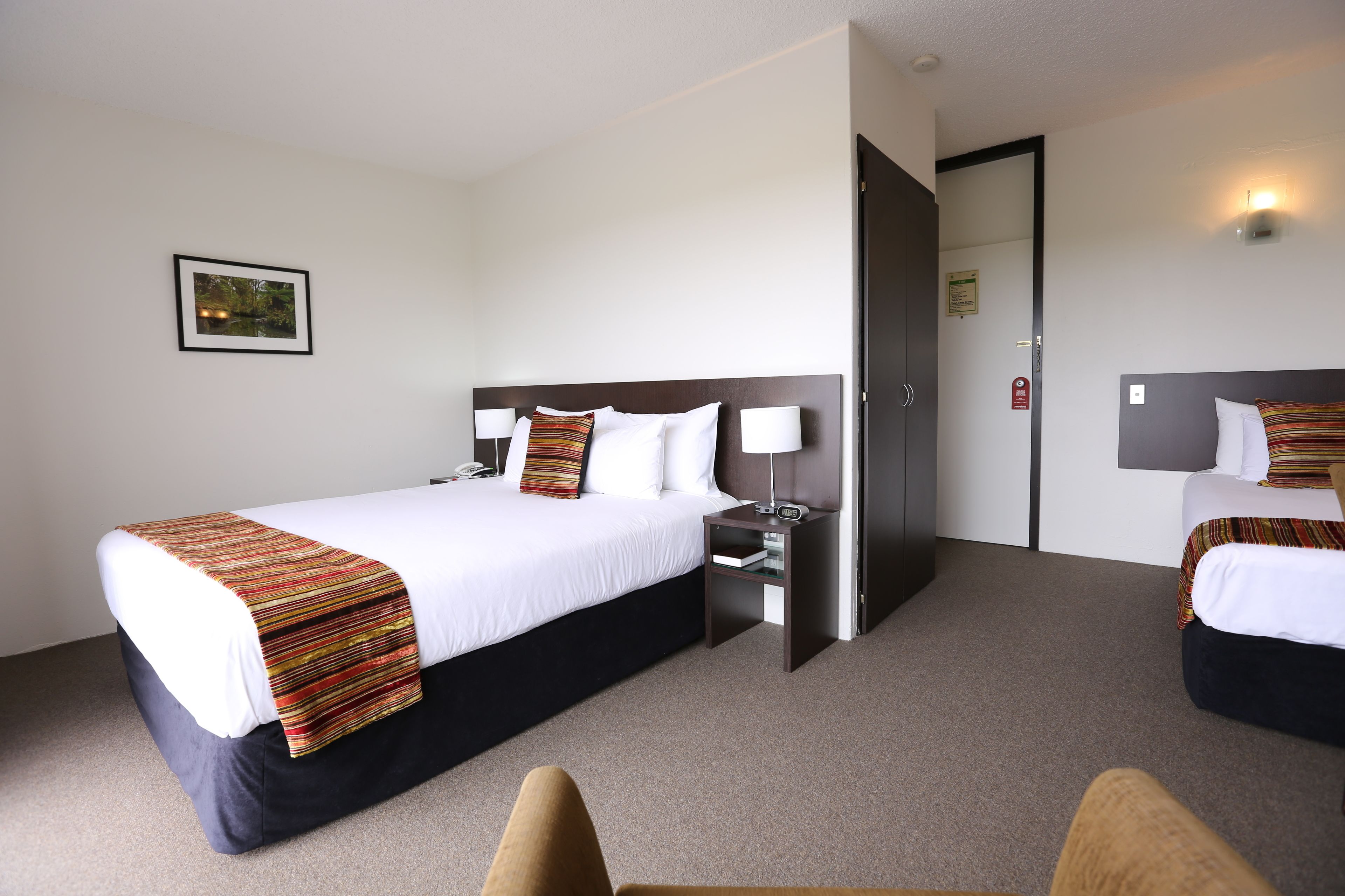 A hotel room with a large bed, two bedside tables, a chair, and a door leading to another room.