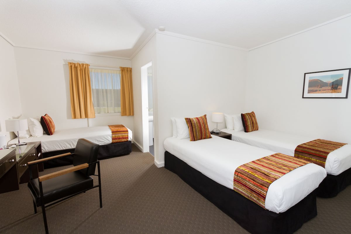 A hotel room with two beds, a desk, a chair, and a window with curtains.