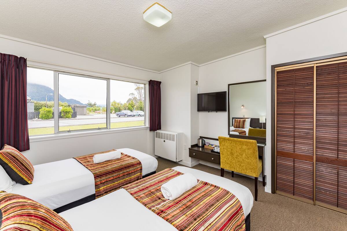 A hotel room with two beds, a desk, a chair, a television, and a large window with a view of the outside.