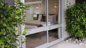 Une chambre d’hôtel dotée d’une porte-fenêtre coulissante, d’un lit avec du linge de maison blanc, d’une table de chevet avec une lampe et d’une vue sur l’intérieur.