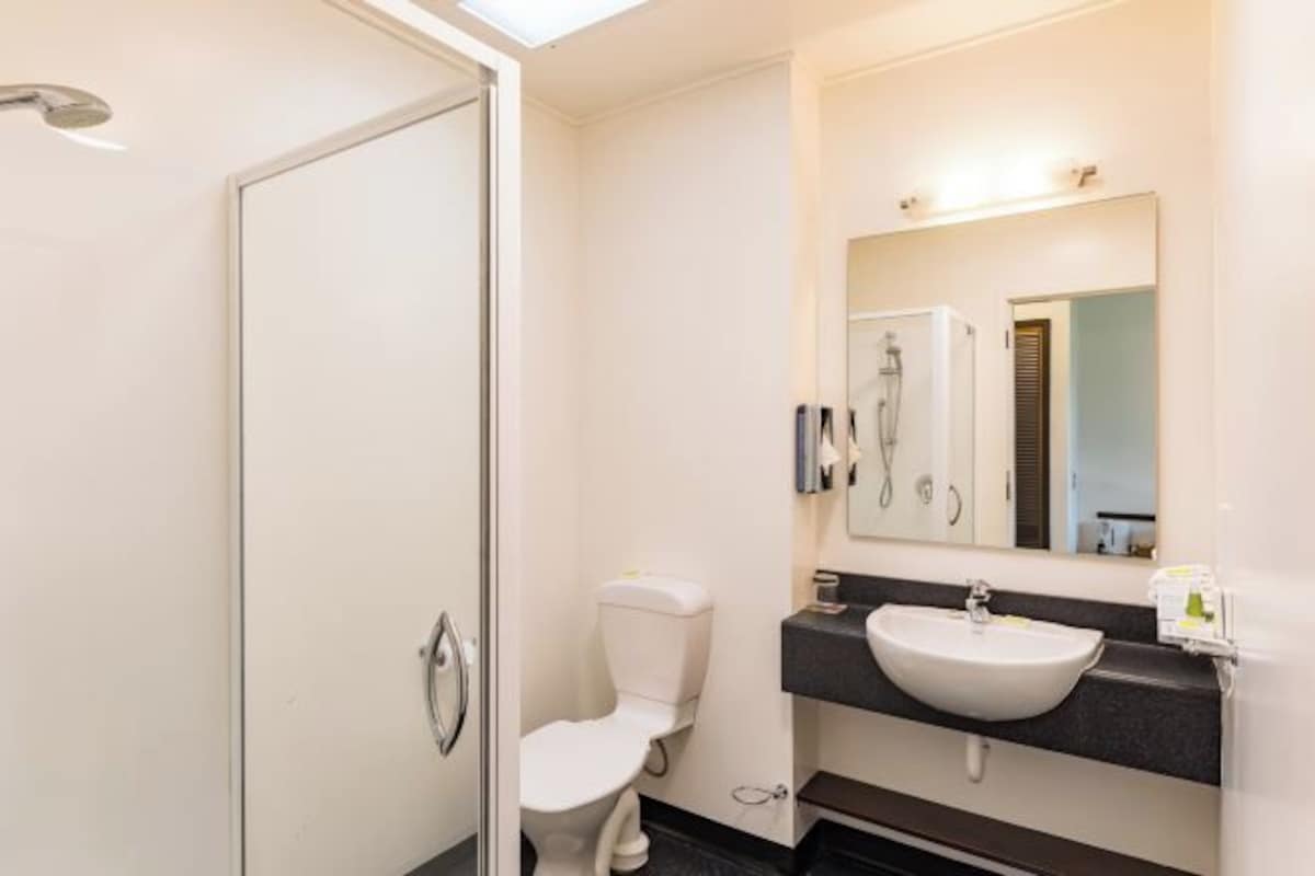 A modern bathroom with a glass shower enclosure, a white toilet, a sink with a dark countertop, and a mirror above the sink.
