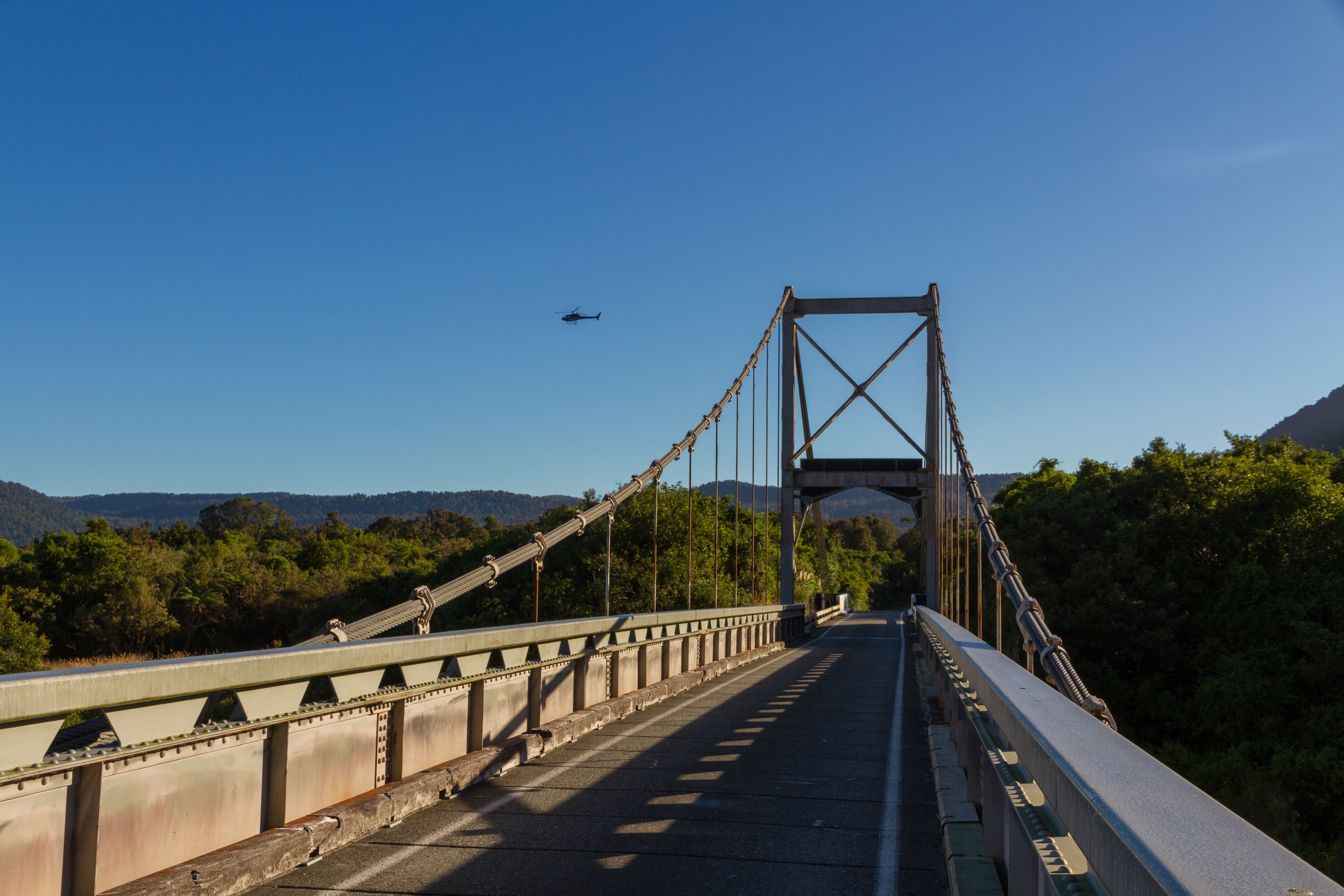Un puente colgante con vistas despejadas del paisaje y un helicóptero a lo lejos.