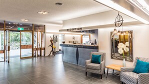 Un espace d’accueil comprenant un comptoir de réception portant les inscriptions « Waiyoto » et « Haast New Zealand », un bureau d’accueil, des chaises à motifs, une petite table et un miroir mural.