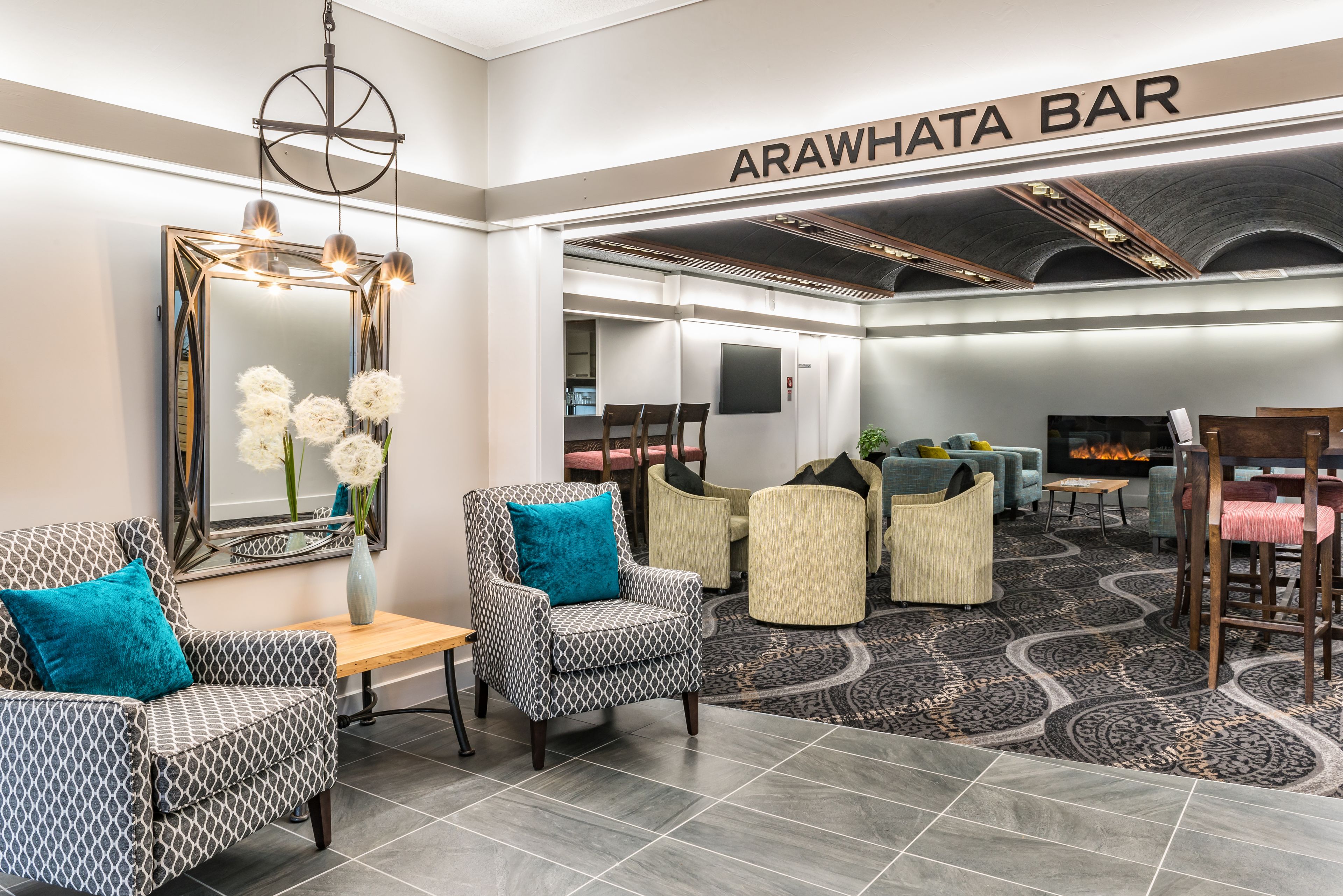 Un vestíbulo con sillas estampadas, un espejo, un jarrón con flores y un cartel que dice "ARAWHATA BAR".
